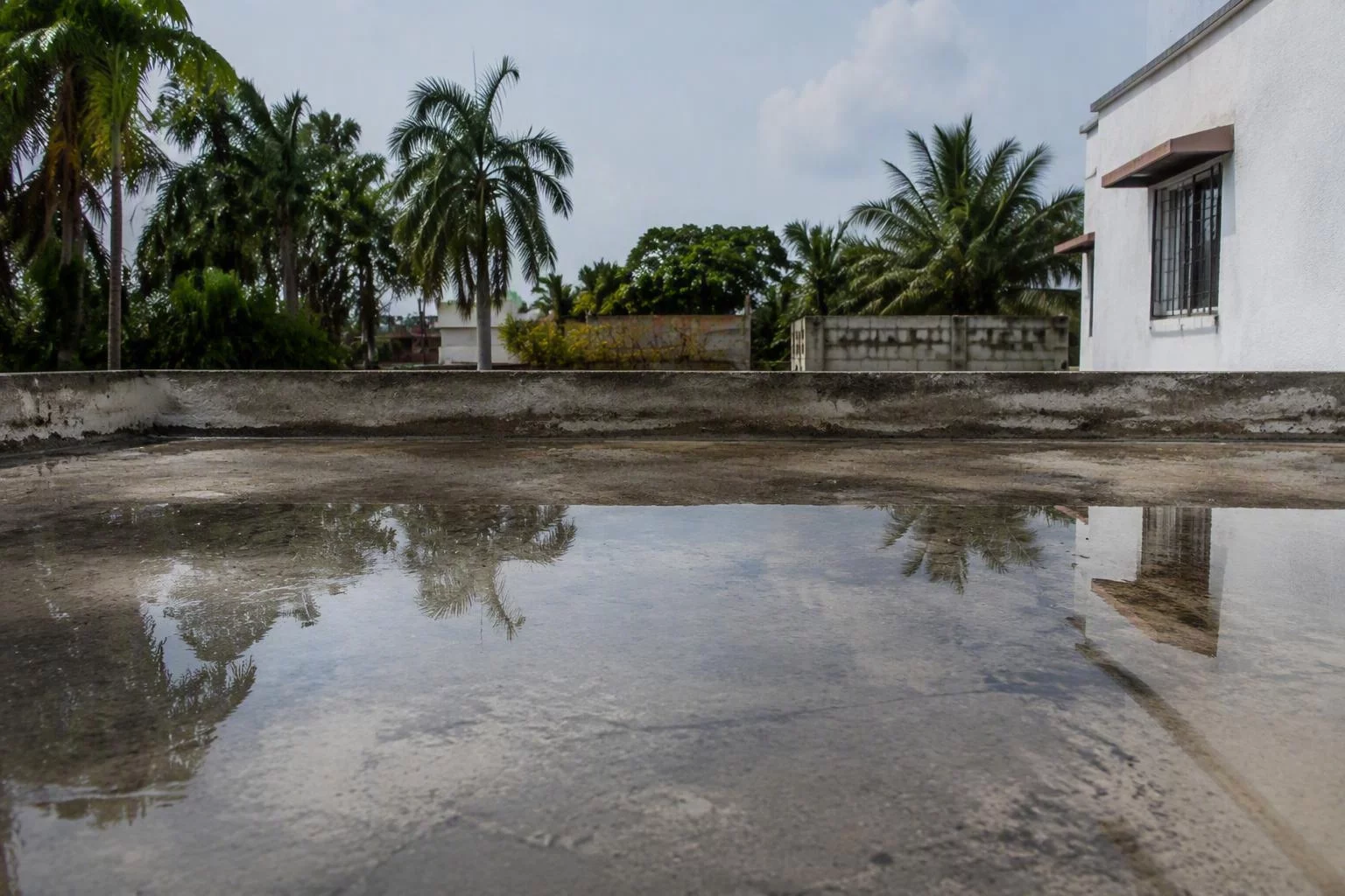 Agua detenida sobre una azotea de concreto después de la lluvia, con el reflejo del cielo y un pretil bajo